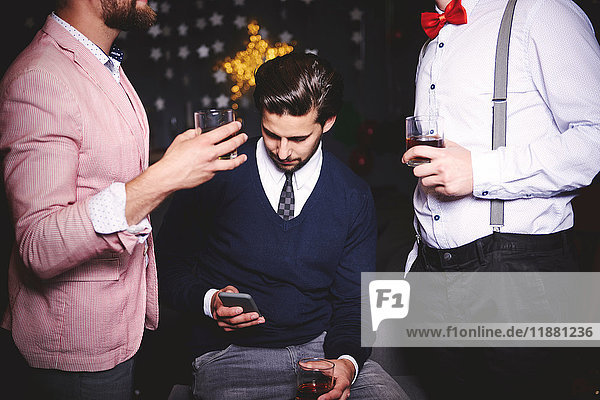 Three men at party  man in middle using smartphone