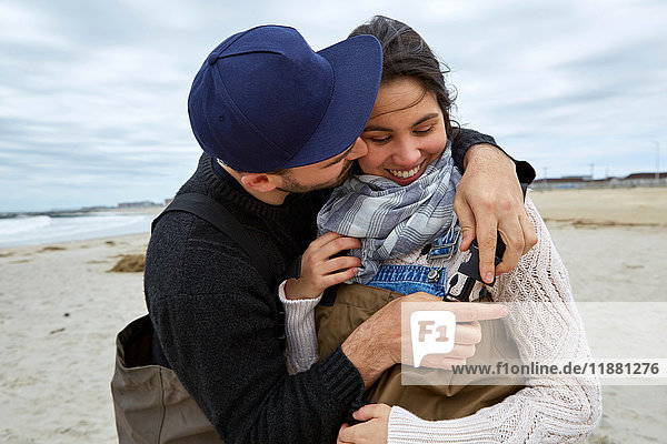 Romantic young sea fishing couple fastening waders on beach
