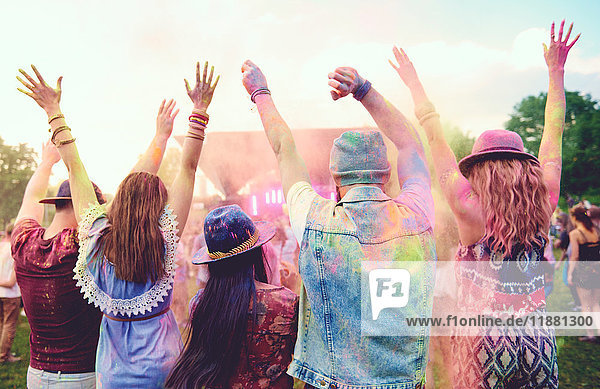 Rear view of young adult friends dancing and throwing coloured chalk powder at festival