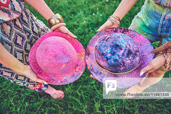 Waist down view of two young women holding felt hats covered in coloured chalk at festival