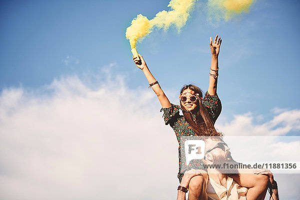 Junge Boho-Frau hält beim Festival gelbe Rauchfackel auf den Schultern ihres Freundes
