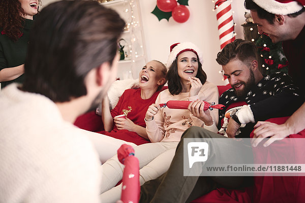 Young adult friends pulling christmas crackers on sofa at christmas party