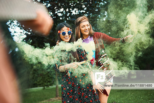Junge Boho-Frauen tanzen mit grüner Rauchfahne auf dem Festival