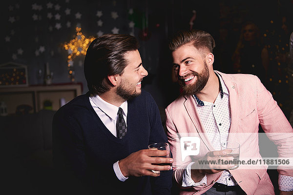Two men at party  holding drinks  laughing