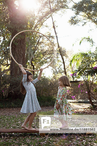 Sisters playing with hula hoop in shaded garden