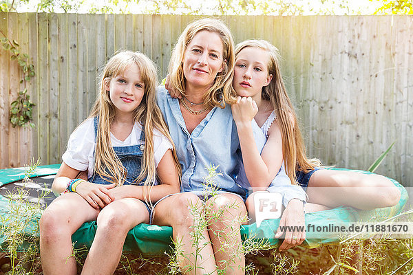 Portrait von Mutter und Töchtern  die auf dem Trampolin sitzen und lächelnd in die Kamera schauen