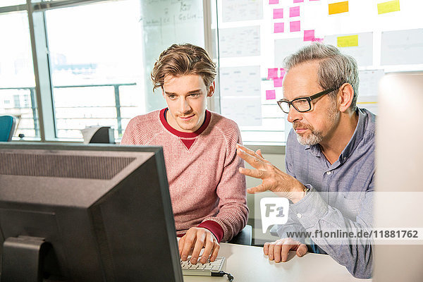 Male digital designer explaining design to trainee at office desk