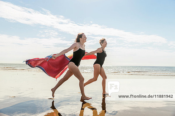 Mutter und Tochter laufen am Strand mit Schals in der Luft  Folkestone  UK