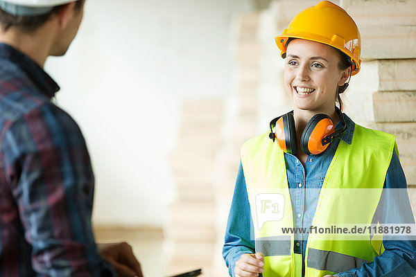 Two people standing in constructions site  wearing hard hats  having discussion