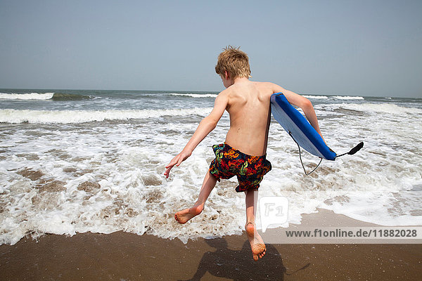 Rear view of boy with bodyboard jumping in sea Goa India Asia