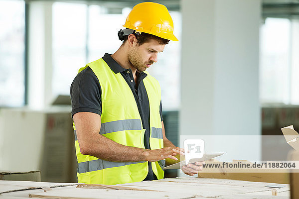 Mann in Hi-Vis-Weste  steht in neu errichtetem Raum und schaut auf ein digitales Tablett