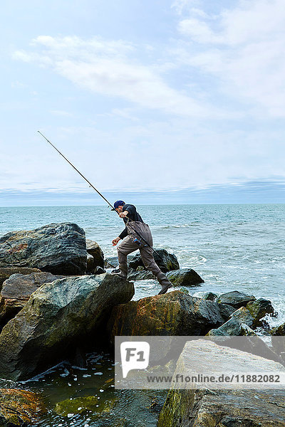 Junger männlicher Seefischer tritt über Strandfelsen