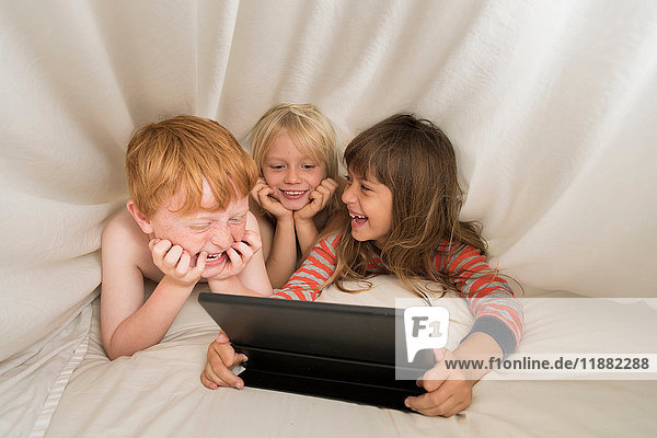 Kinder liegen im Bett und schauen auf das digitale Tablett