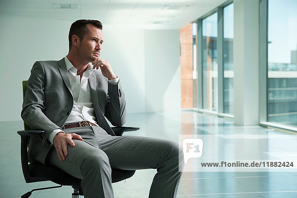 Geschäftsmann sitzt auf einem Stuhl im leeren Büroraum  nachdenklicher Ausdruck