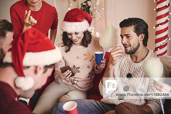 Young women and men looking at smartphone on sofa at christmas party