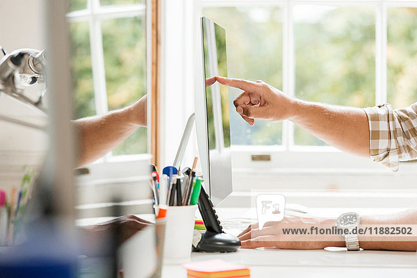 Hand eines männlichen Designers die auf einen Desktop-Computer im Kreativstudio zeigt