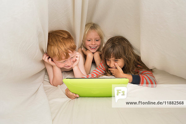 Children lying in bed looking at digital tablet