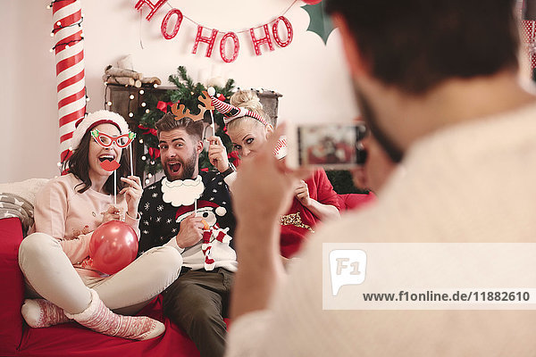 Over shoulder view of young man photographing friends on sofa at christmas party