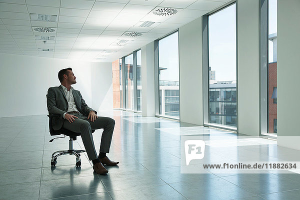 Geschäftsmann sitzt auf einem Stuhl in einem leeren Büro und schaut aus dem Fenster
