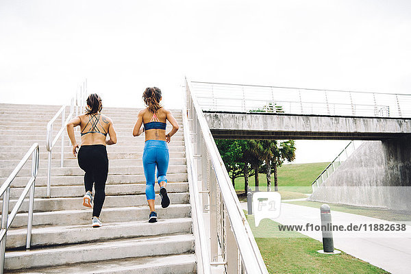 Two you women exercising outdoors running up steps rear view steps South Point Park Miami Beach Florida USA