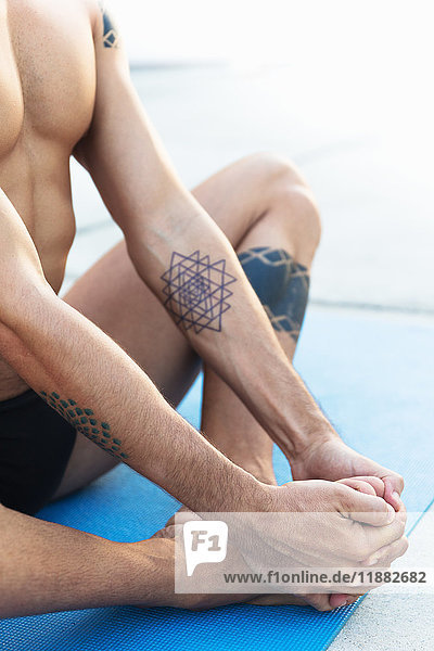 Schrägansicht eines Yoga praktizierenden Mannes  der in Lotus-Position auf einer Yogamatte sitzt