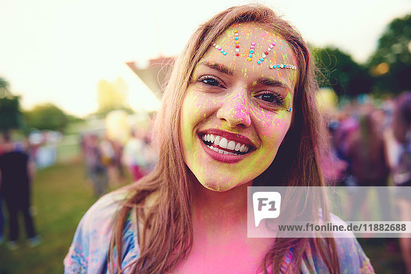 Portrait of young boho woman with face covered in coloured chalk powder at festival