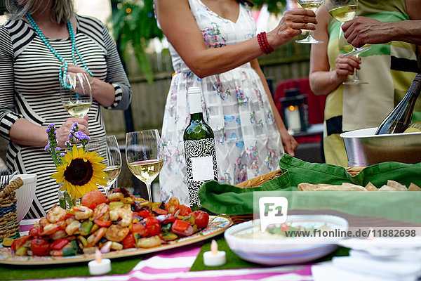 Personengruppe beim Gartenfest  Weingläser halten  Toast ausbringen  Essen auf Servierplatten auf dem Tisch  Mittelteil