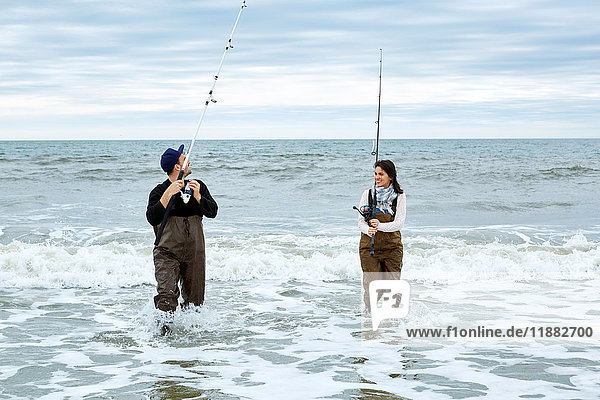 Young couple in waders sea fishing knee deep in water