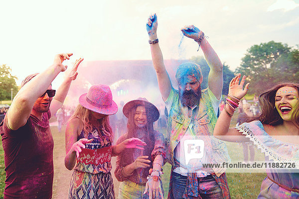 Junge erwachsene Freunde tanzen und werfen farbiges Kreidepulver auf das Festival