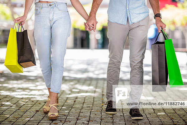 Young couple outdoors  holding hands  holding shopping bags  low section