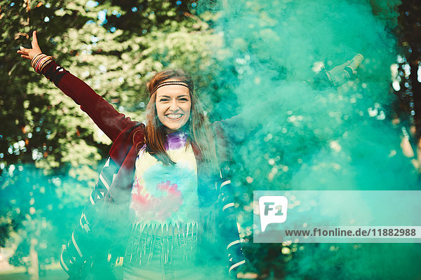 Young boho woman dancing with green smoke flare at festival