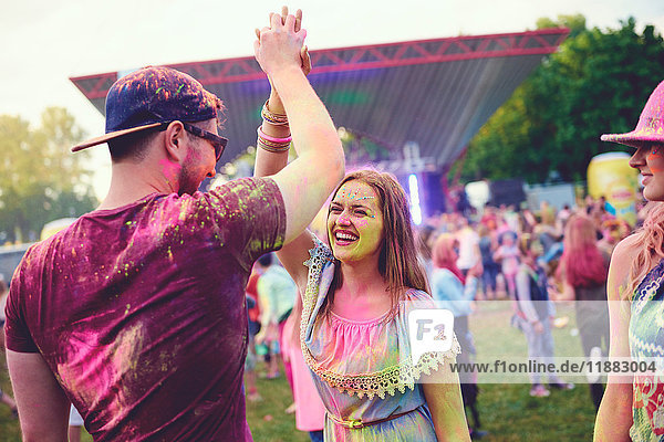 Young adults covered in coloured chalk powder high fiving at festival