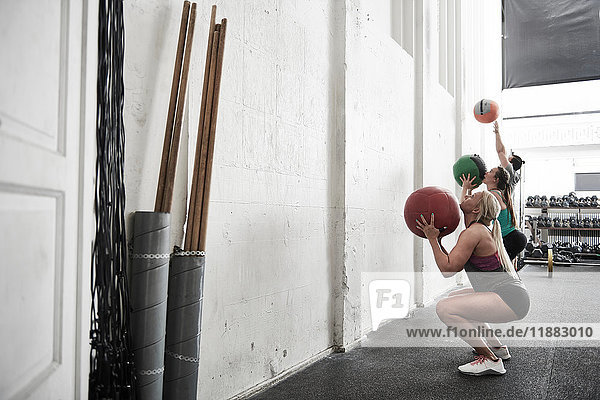 Friends throwing fitness ball against wall in cross training gym