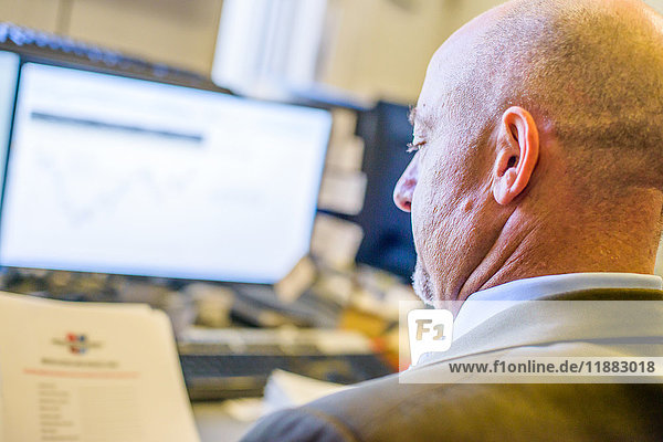 Über-Schulter-Ansicht eines Geschäftsmannes beim Lesen von Papierkram am Büroschreibtisch