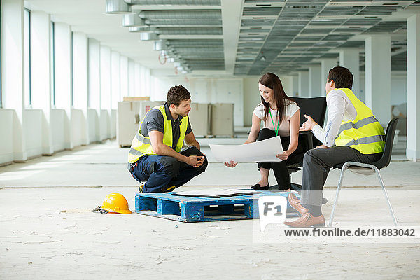 Three people sitting in newly constructed office space  looking at construction plans