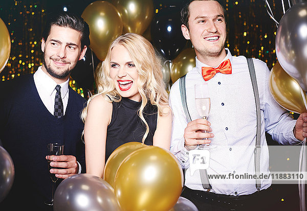 Portrait of three people at party  surrounded by balloons  holding champagne glasses