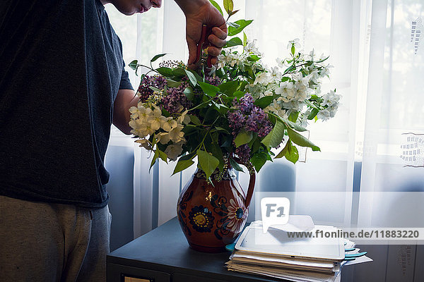 Mid section of young man arranging vase of flowers in front of window