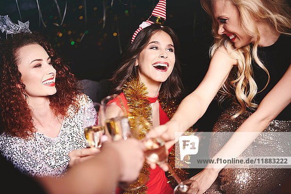Drei Frauen sitzen auf einer Party zusammen  halten Champagnergläser in der Hand und bringen einen Toast aus