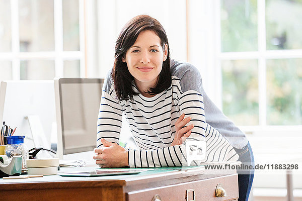 Portrait of female designer leaning forward on drawers in creative studio