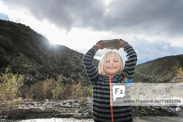 Portrait of cute boy holding up rock from riverbed