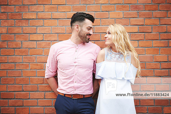 Portrait of couple in front of brick wall face to face smiling