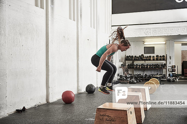 Woman jumping onto fitness box in cross training gym
