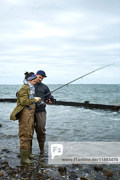 Young man ankle deep in water teaching girlfriend sea fishing