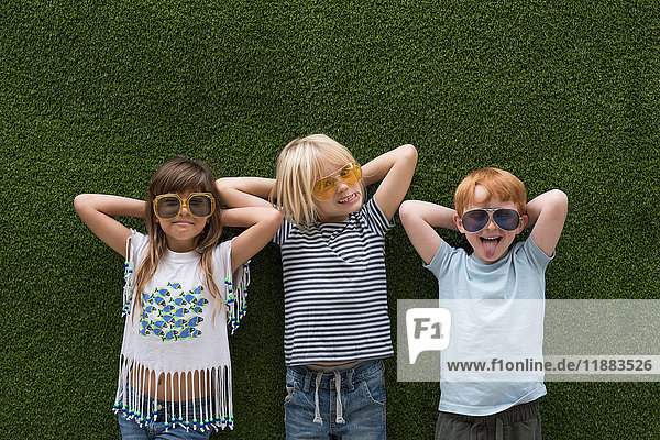 Children in front of artificial turf wall hand behind head wearing sunglasses