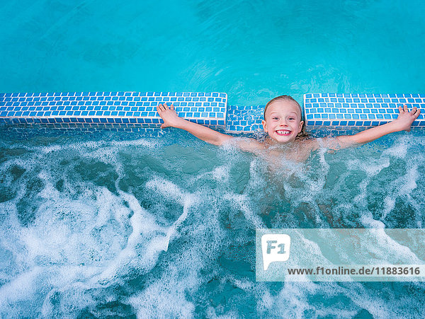 Overhead portrait of cute boy splashing in outdoor swimming pool