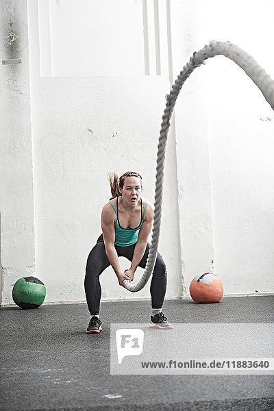 Woman working out with battle rope in cross training gym