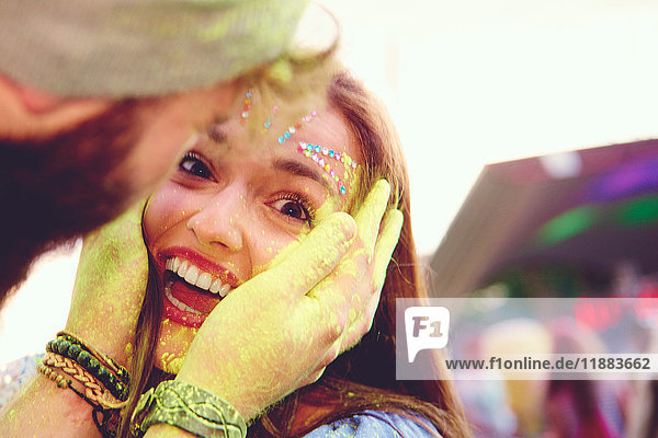 Portrait of young woman and boyfriend cupping her face with yellow chalked hand at festival