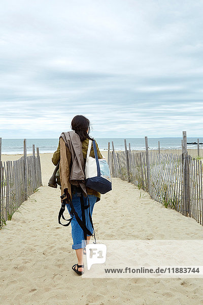 Rear view of young woman carrying sea fishing equipment on beach