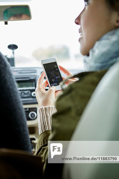 Young couple sitting in car  woman holding smartphone  rear view