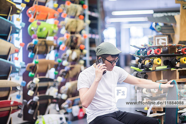Junger männlicher Skateboarder telefoniert mit seinem Smartphone im Skateboard-Shop